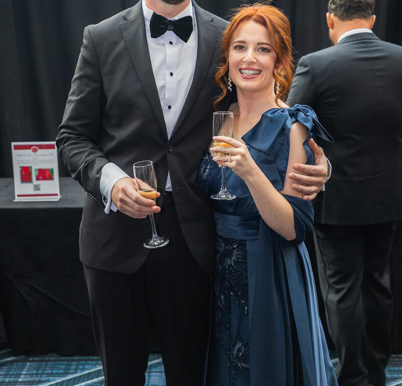 Smiling couple in formal attire toasting with champagne at a black-tie event.