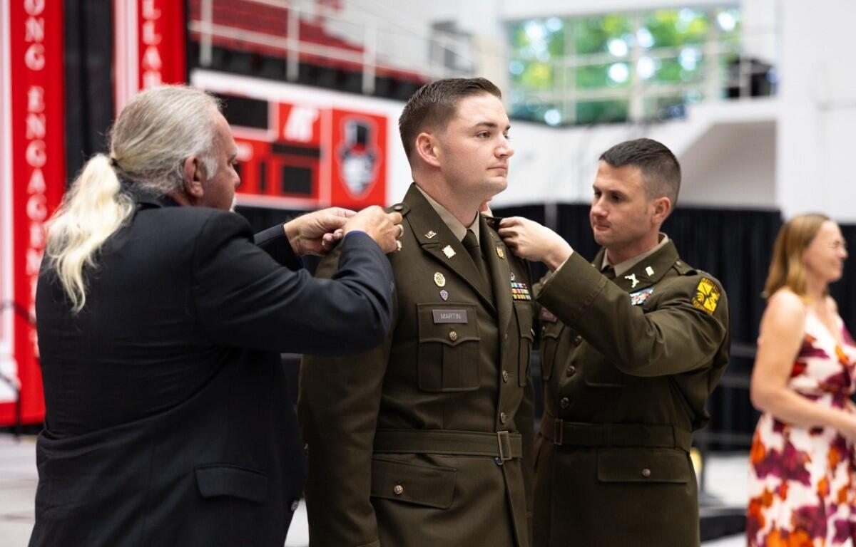 Soldier in dress uniform being pinned by an older man as another officer assists, during a ceremony (name tag 'MARTIN' visible).