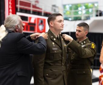 Soldier in dress uniform being pinned by an older man as another officer assists, during a ceremony (name tag 'MARTIN' visible).