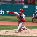 Right-handed pitcher in gray and red delivers a pitch from the mound during a daytime baseball game.