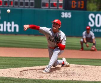 Right-handed pitcher in gray and red delivers a pitch from the mound during a daytime baseball game.