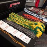 Table with award medals on green and yellow cords, red/white/blue lanyards, and white drawstring bags at a university event with branding in the background.