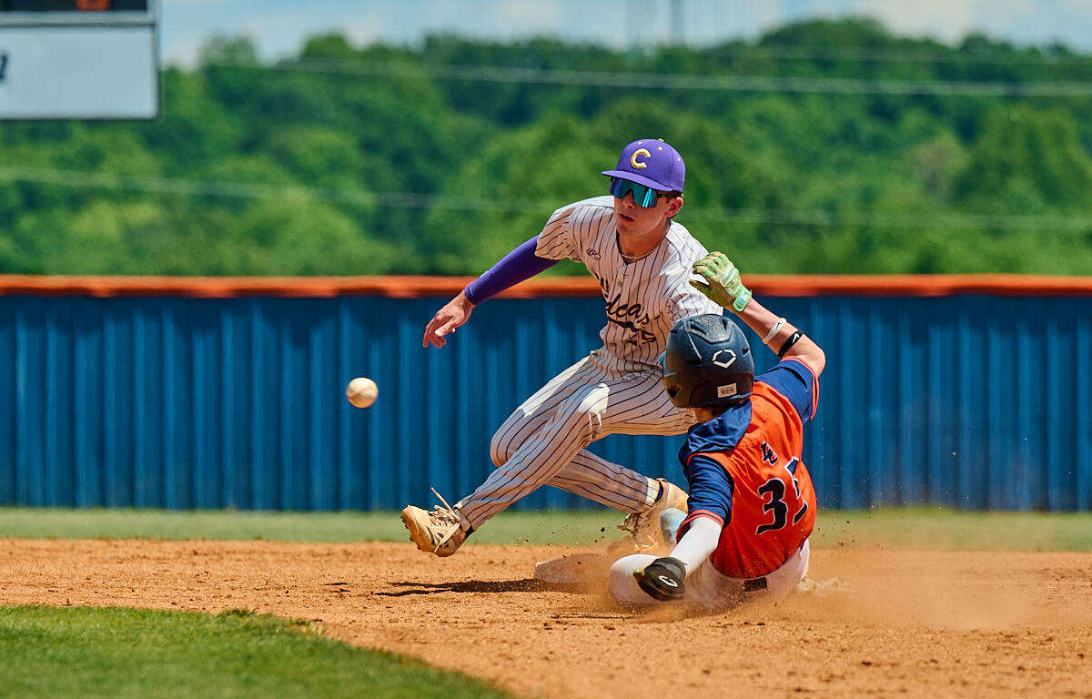 Baseball scene: runner in orange and blue slides into a base while the fielder in pinstripe attempts a tag; ball is bouncing nearby on the dirt.