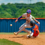 Baseball scene: runner in orange and blue slides into a base while the fielder in pinstripe attempts a tag; ball is bouncing nearby on the dirt.