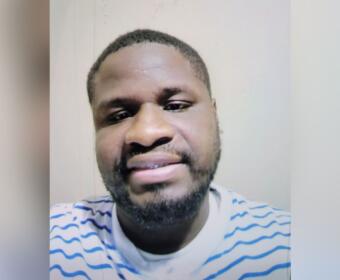 Close-up portrait of a man with short hair and a beard, wearing a white shirt with blue stripes, looking at the camera.