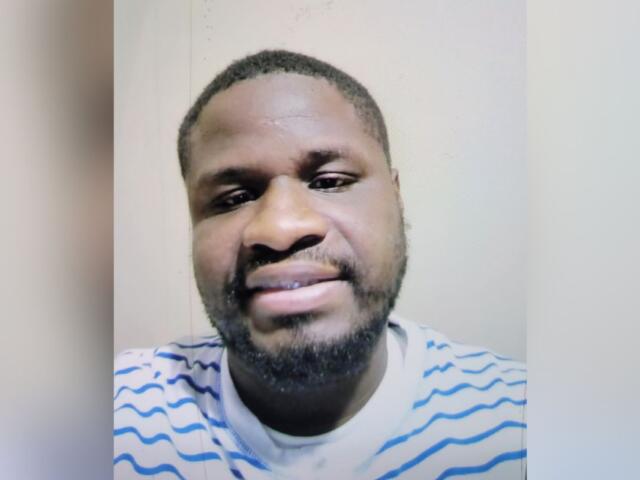Close-up portrait of a man with short hair and a beard, wearing a white shirt with blue stripes, looking at the camera.