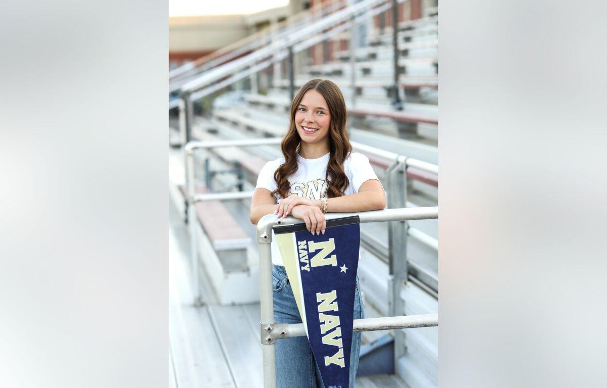 Smiling young woman leaning on a railing with a navy pennant hanging over the rail in a stadium setting.
