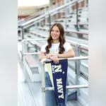 Smiling young woman leaning on a railing with a navy pennant hanging over the rail in a stadium setting.