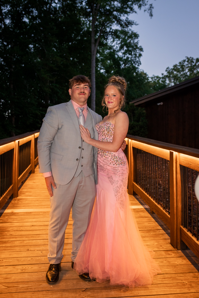 Couple in formal wear posing on a warmly lit wooden bridge at dusk outdoor setting.