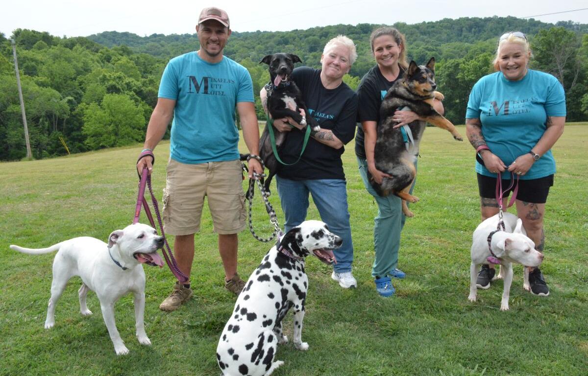 Group of five adults in a field with several dogs, smiling for the photo.