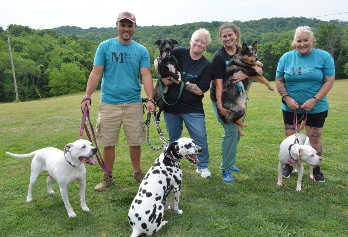Group of five adults in a field with several dogs, smiling for the photo.