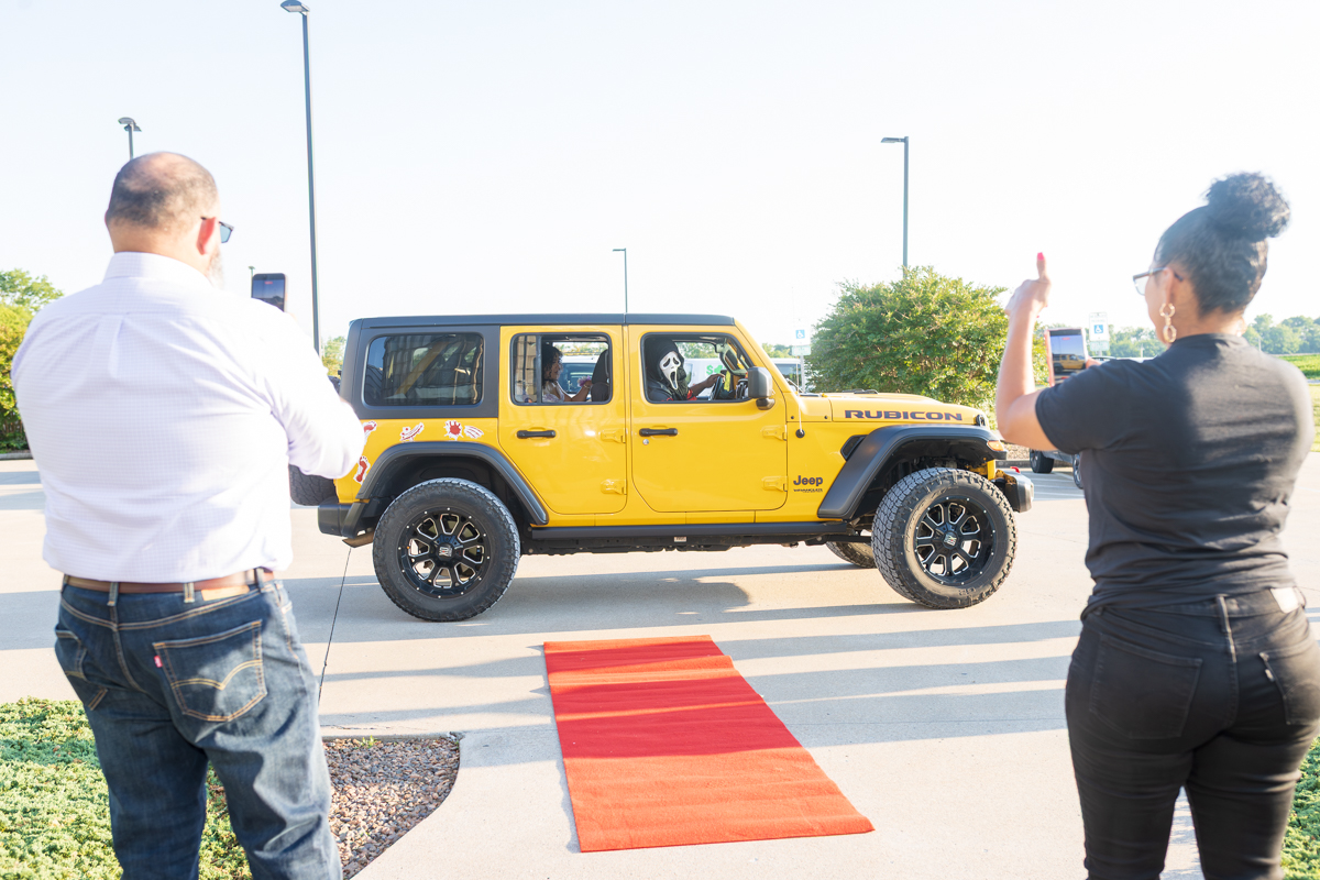 Yellow Jeep Wrangler Rubicon on a red carpet, with two people taking photos outdoors in a parking lot.
