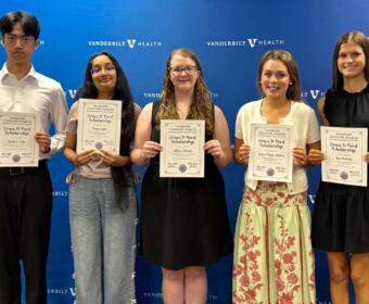 Five students stand in a row holding Grace P. Ford Scholarship certificates in front of a Vanderbilt Health backdrop.