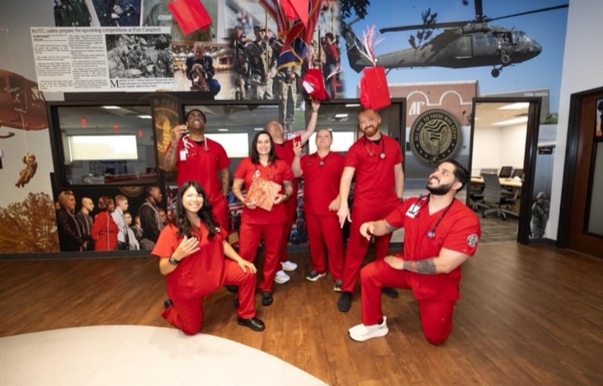 Group of seven people in red scrubs pose celebrating in a hallway with a helicopter mural behind them named and a circular emblem on the wall.