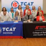 Group of ten professionals at a signing event, seated and standing behind two tables with TCAT Dickson and APSU banners in a classroom setting.