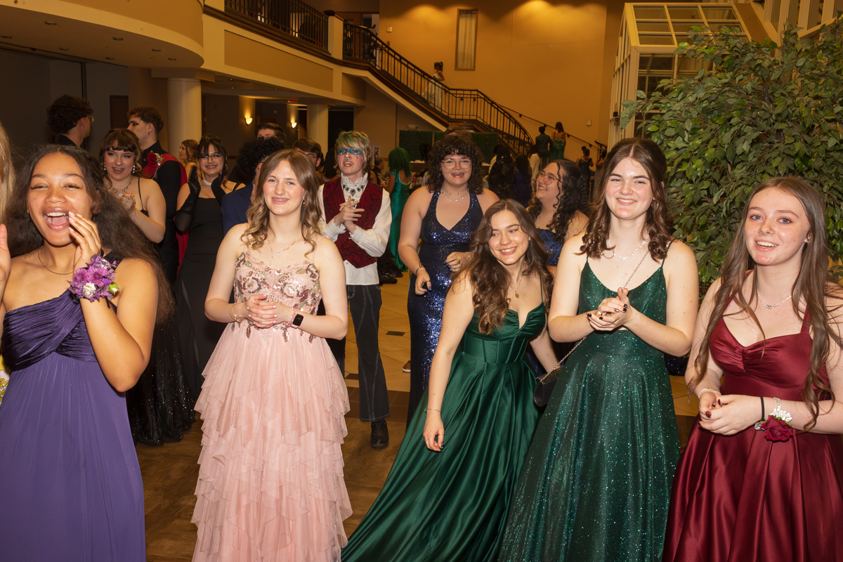 Group of teenagers in formal gowns standing in a banquet hall, smiling and chatting at a school dance.