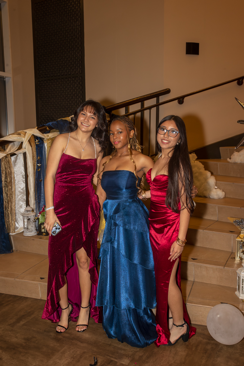 Three women in formal gowns posing together on a staircase at a party venue.