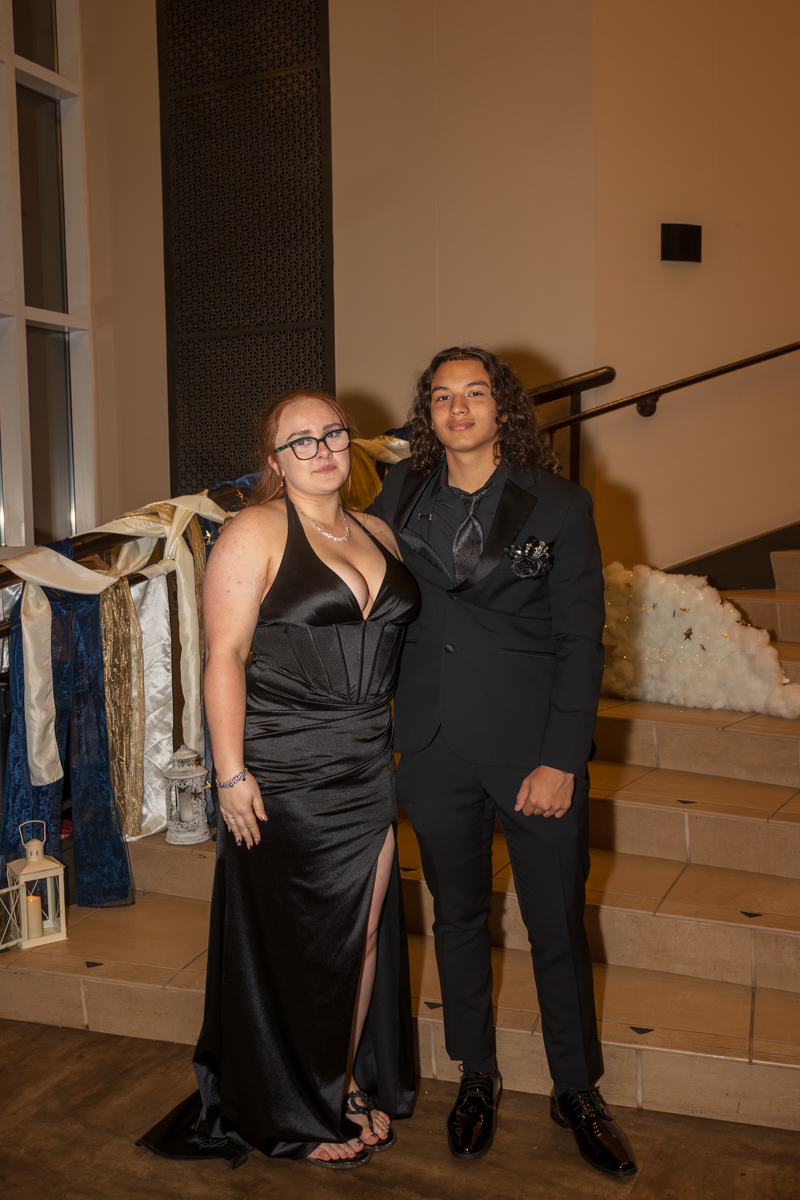 Two young adults in formal attire pose together on a staircase at a gala or formal event.