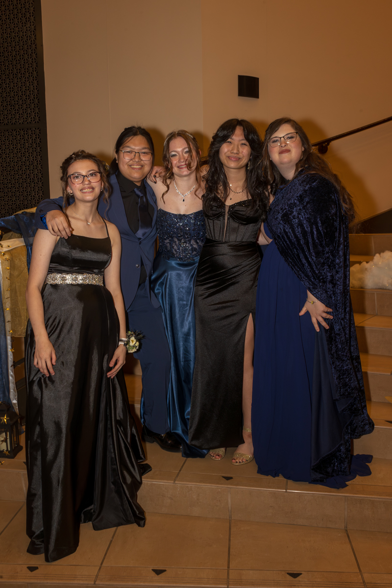 Five friends in formal attire pose together on a staircase at a formal event.