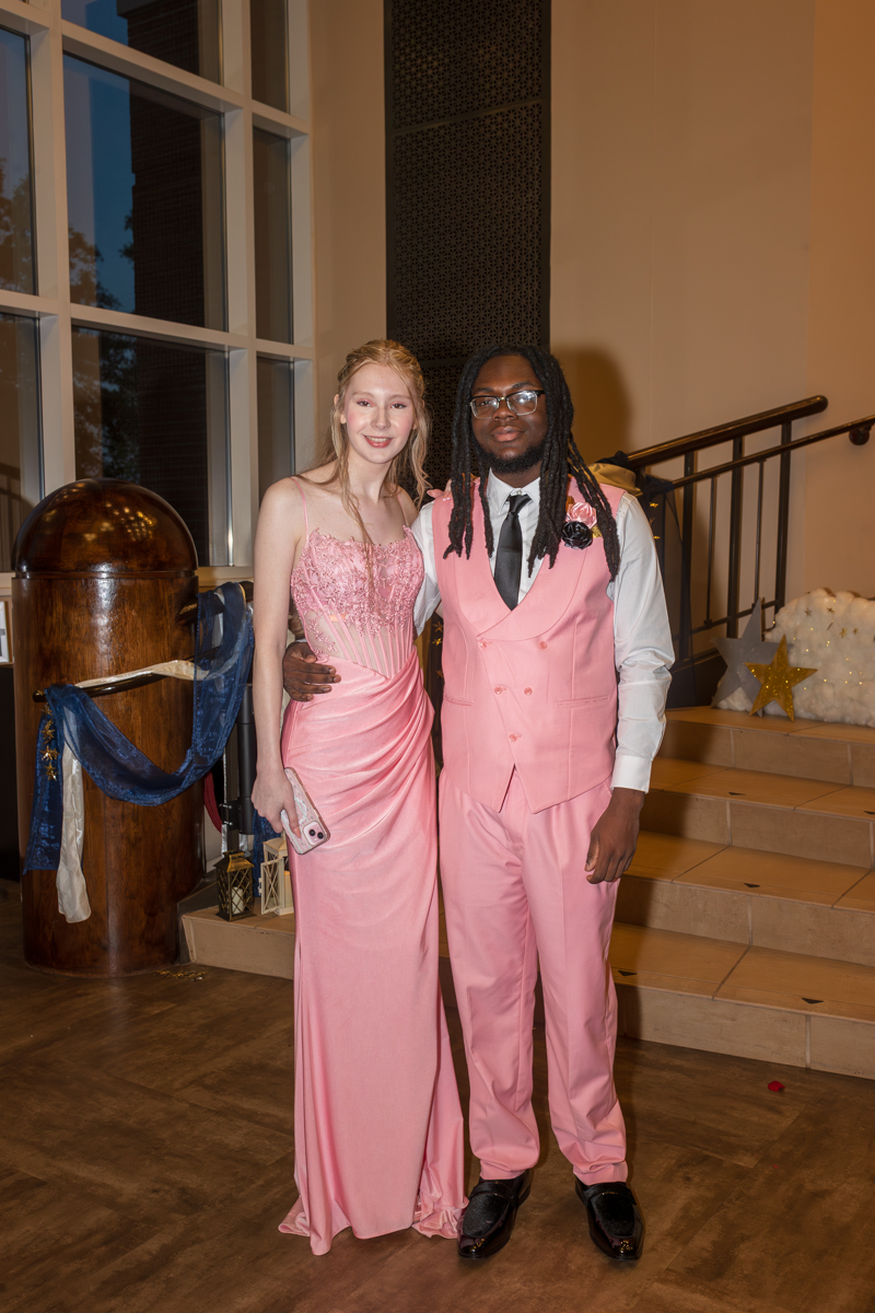 Couple in matching pink formal wear posing together indoors near a staircase.