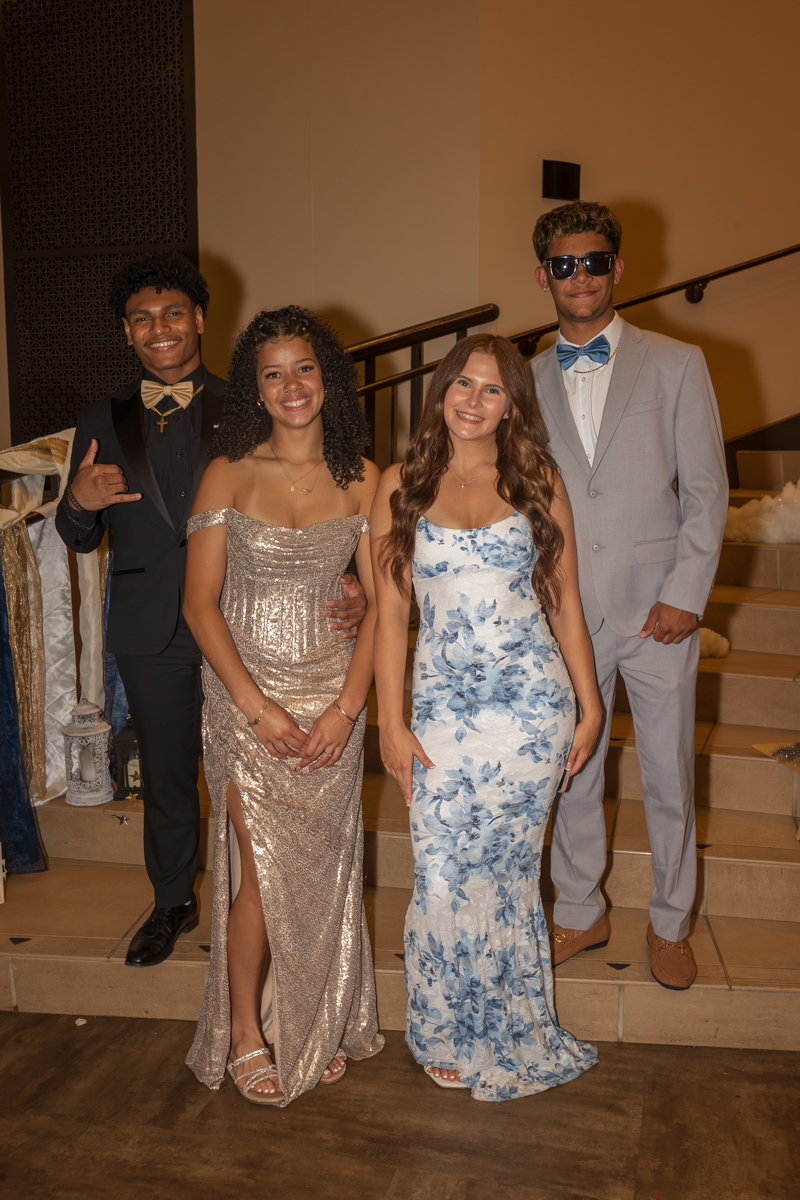 Four friends in formal attire posing on a staircase at a social event, smiling at the camera.