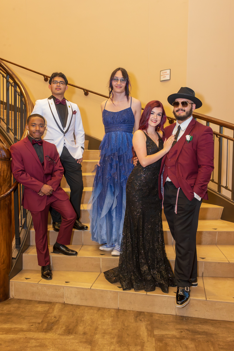 Five people in formal attire posing on a staircase indoors at an event area.