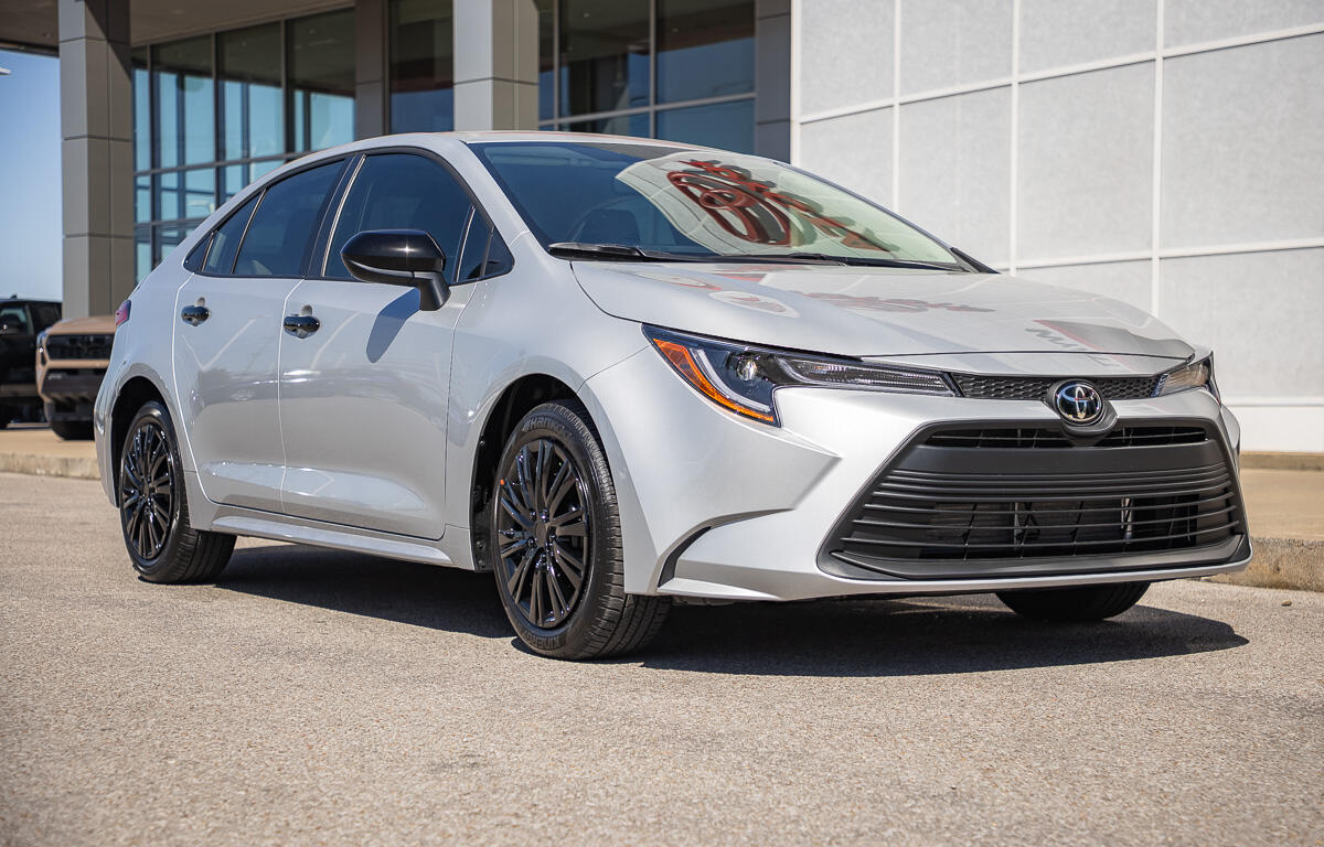 Silver Toyota Camry parked outside a modern dealership, shown in a front three-quarter view.