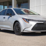 Silver Toyota Camry parked outside a modern dealership, shown in a front three-quarter view.