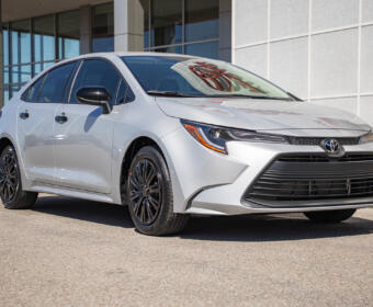 Silver Toyota Camry parked outside a modern dealership, shown in a front three-quarter view.