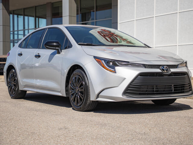 Silver Toyota Camry parked outside a modern dealership, shown in a front three-quarter view.