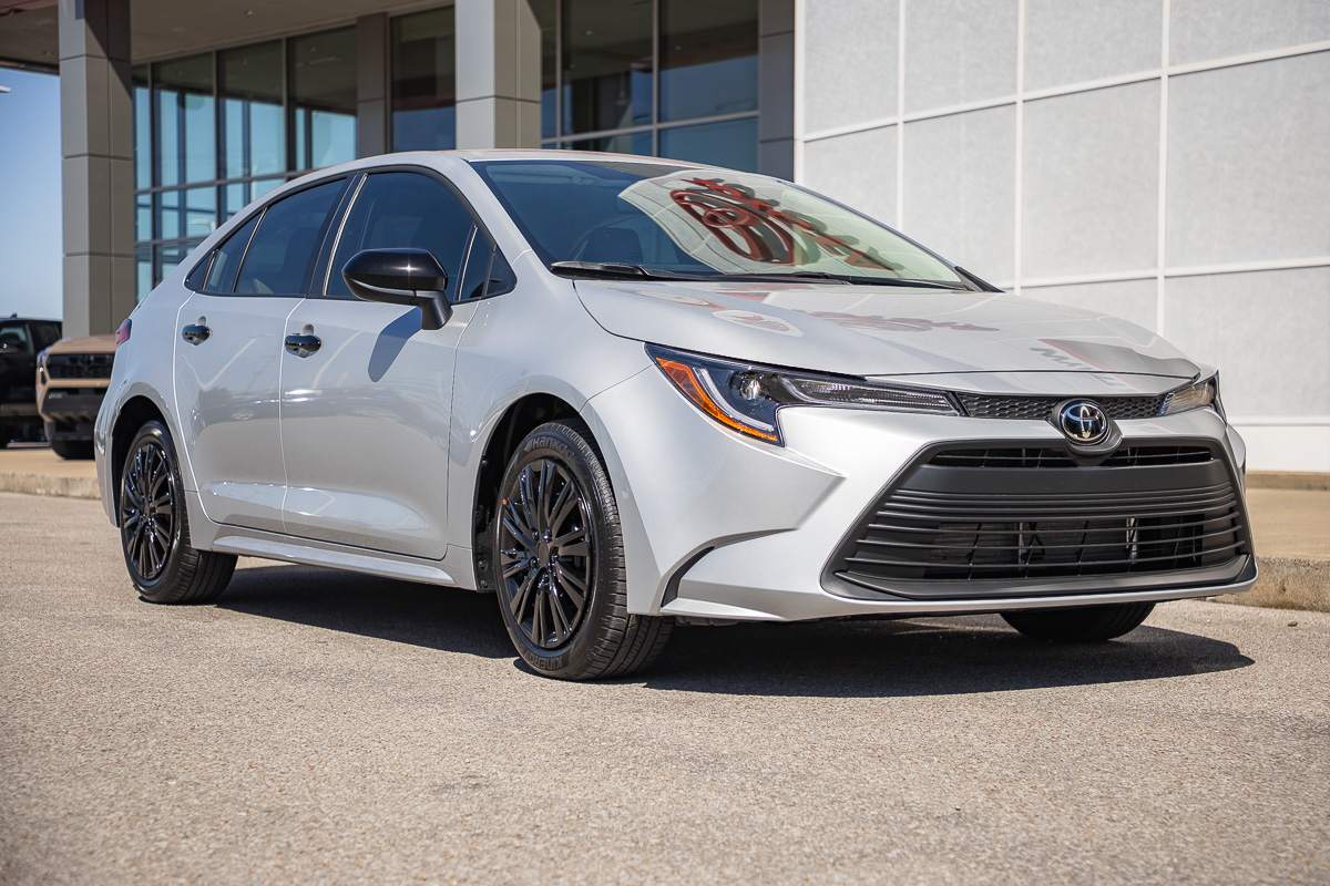 Silver Toyota Camry parked outside a modern dealership, shown in a front three-quarter view.