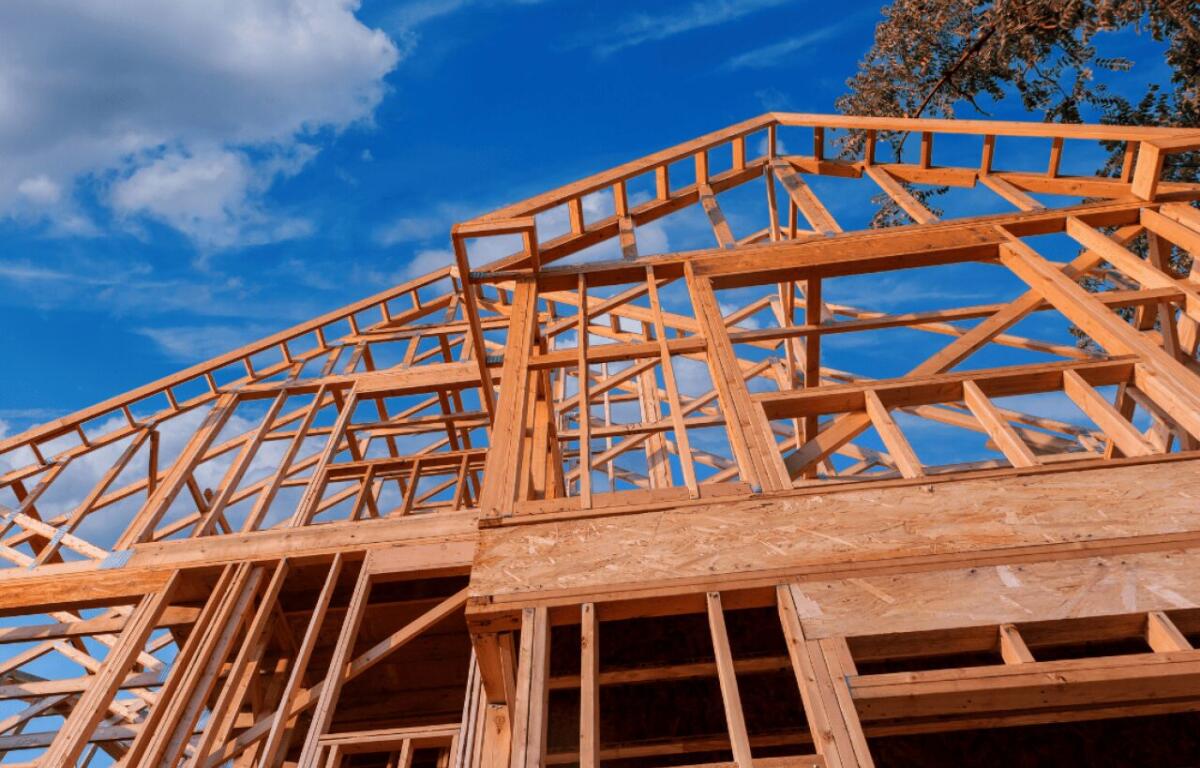 Timber-frame house under construction against a clear blue sky.
