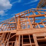 Timber-frame house under construction against a clear blue sky.
