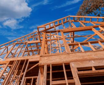 Timber-frame house under construction against a clear blue sky.