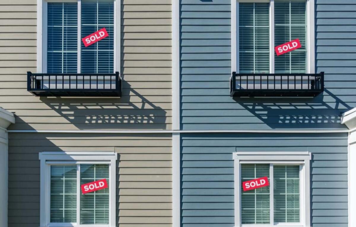 Four exterior windows on a beige and blue duplex with red SOLD signs in the panes, indicating sold properties in each unit.