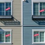 Four exterior windows on a beige and blue duplex with red SOLD signs in the panes, indicating sold properties in each unit.