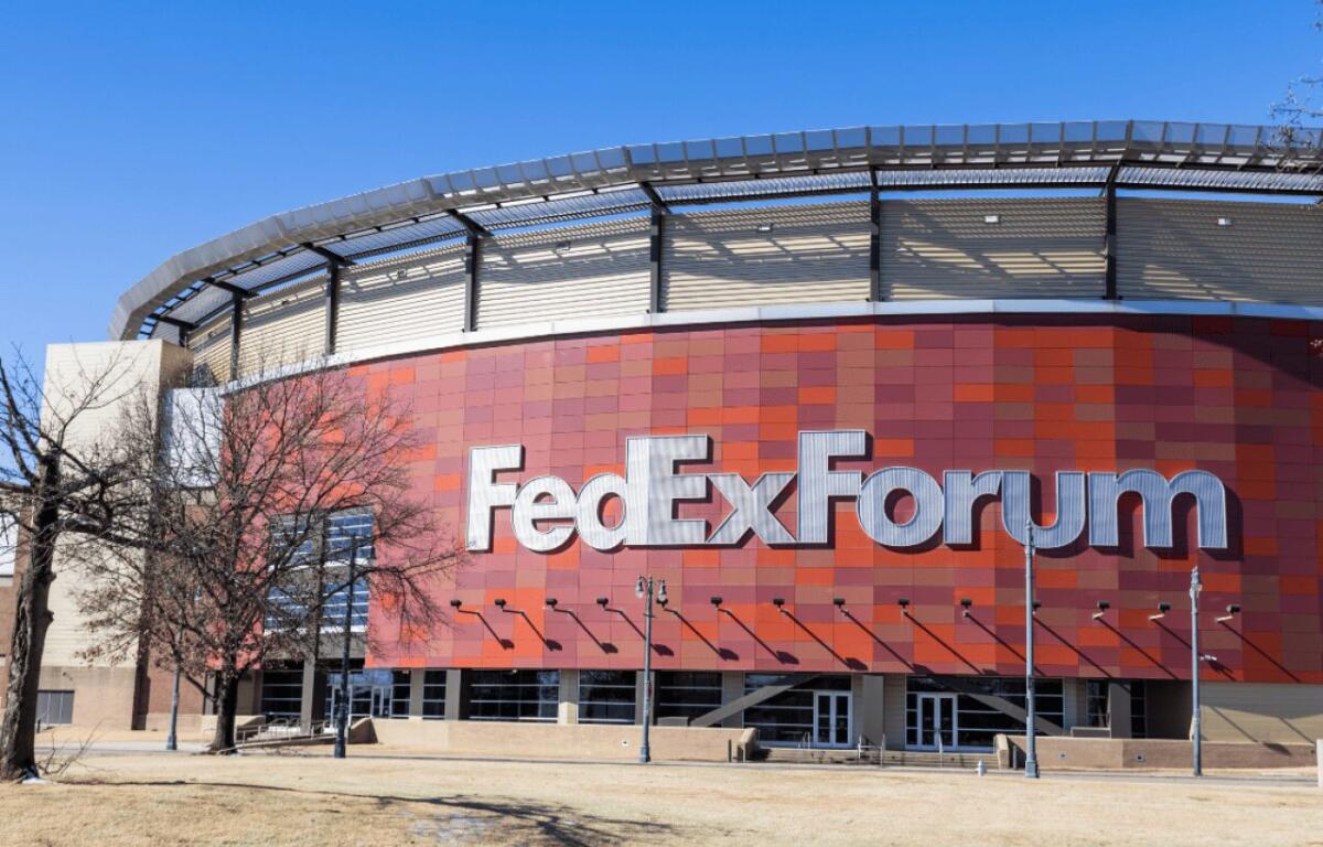 Exterior of the FedExForum arena with a red tiled facade and large silver ‘FedExForum’ letters against a bright blue sky.