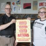 Two adults stand side by side and hold a poster promoting strong communities and nations at a university setting.