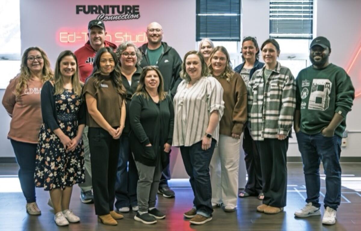 Group of coworkers posing for a photo in a modern office setting with a neon sign on the wall behind them (FURNITURE Connection).