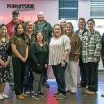 Group of coworkers posing for a photo in a modern office setting with a neon sign on the wall behind them (FURNITURE Connection).