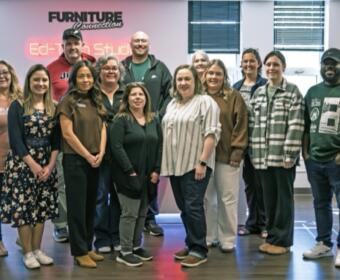 Group of coworkers posing for a photo in a modern office setting with a neon sign on the wall behind them (FURNITURE Connection).