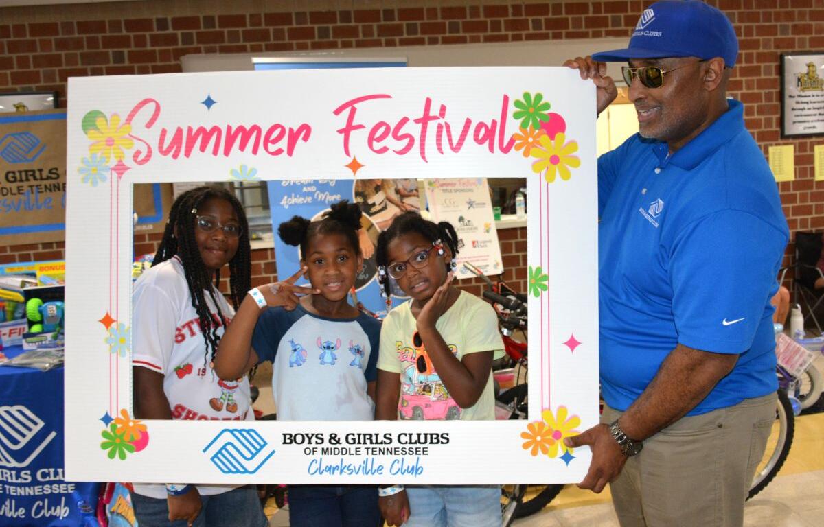 Three girls pose inside a colorful 'Summer Festival' frame with a man in a blue polo at a Boys & Girls Clubs event in Clarksville, Tennessee.