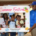 Three girls pose inside a colorful 'Summer Festival' frame with a man in a blue polo at a Boys & Girls Clubs event in Clarksville, Tennessee.
