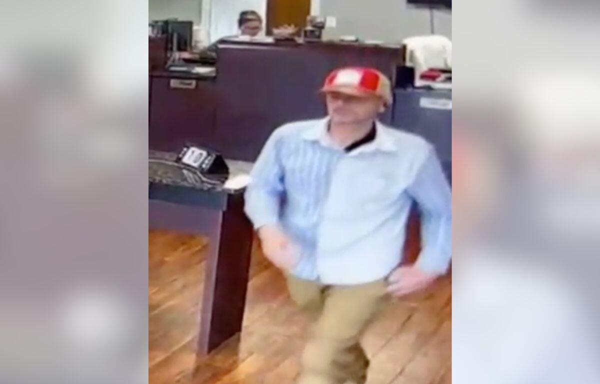 Man in a red-and-white striped cap and light blue shirt standing near a bank counter.