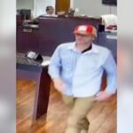 Man in a red-and-white striped cap and light blue shirt standing near a bank counter.