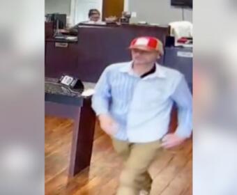 Man in a red-and-white striped cap and light blue shirt standing near a bank counter.
