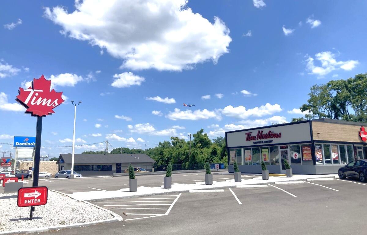 Tim Hortons storefront in a parking lot under a bright blue sky with a small plane in the distance.