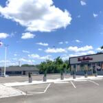 Tim Hortons storefront in a parking lot under a bright blue sky with a small plane in the distance.
