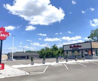 Tim Hortons storefront in a parking lot under a bright blue sky with a small plane in the distance.