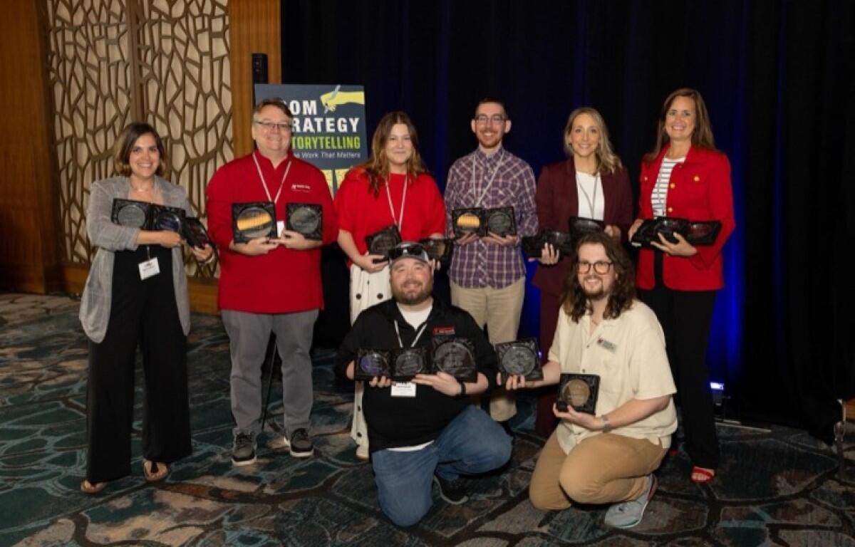Eight people pose indoors with award plaques at a ceremony, smiling for the photo.